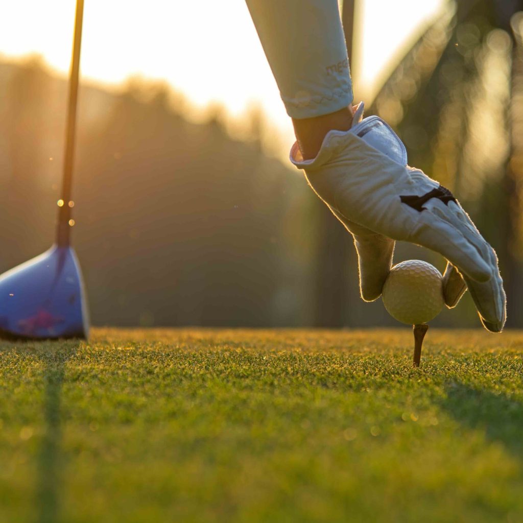 Hand asian woman putting golf ball on tee with club in golf course on evening and sunset time a for healthy sport.  Lifestyle Concept