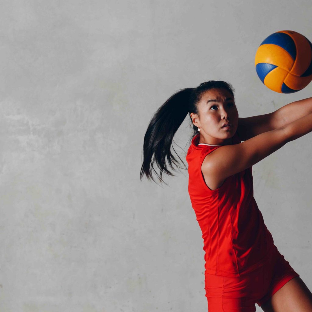 Young Asian woman volleyball player in red uniform takes ball